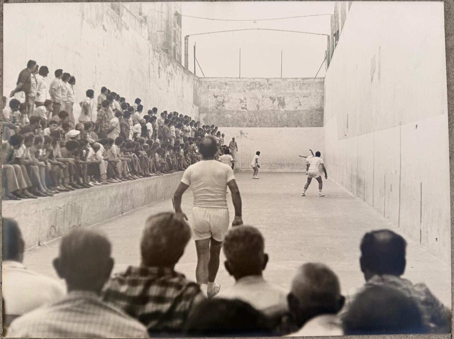 Foto antiga del trinquet: Una partida de raspall amb la grada plena